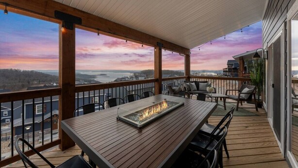 A covered outdoor deck with a fire feature, seating, and a view of the landscape. - Gorgeous Lake View | Indoor Pool Access | Hot Tub (Branson)