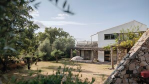 A modern house with a stone wall, a patio, and a garden with trees and shrubs. - Cabana Apartment with Shared Pool (Castelo de Vide)