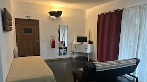 A room with a bed, a desk with a computer, a chair, a fire extinguisher, and a window with curtains. - Cabana Apartment with Shared Pool (Castelo de Vide)