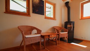 A room with two wicker chairs, a wooden table, a black wood-burning stove, and large windows. - Melody - Joli 2 pièces | La Sage (La Sage)