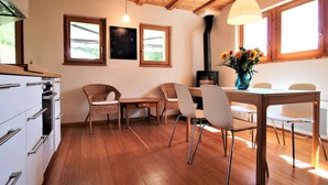 A modern kitchen with wooden cabinets, a dining area with wicker chairs, and a large window with a view. - Melody - Joli 2 pièces | La Sage (La Sage)