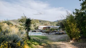 Une maison avec une piscine, entourée d’une végétation luxuriante et de collines.