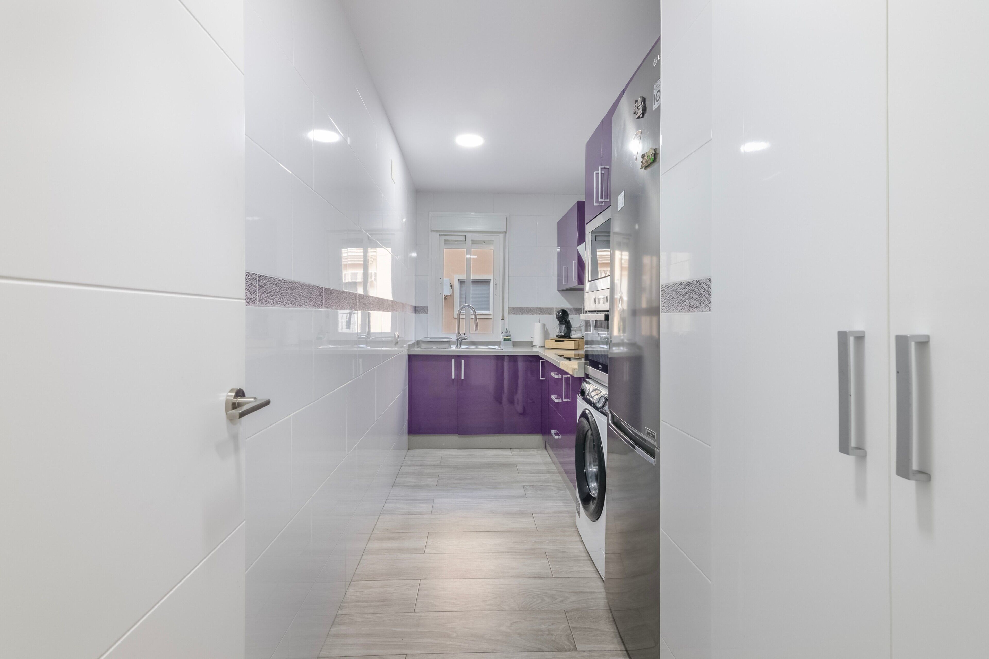 Eine moderne Küche mit weißen und violetten Schränken, einem Edelstahlkühlschrank und einer Waschmaschine.