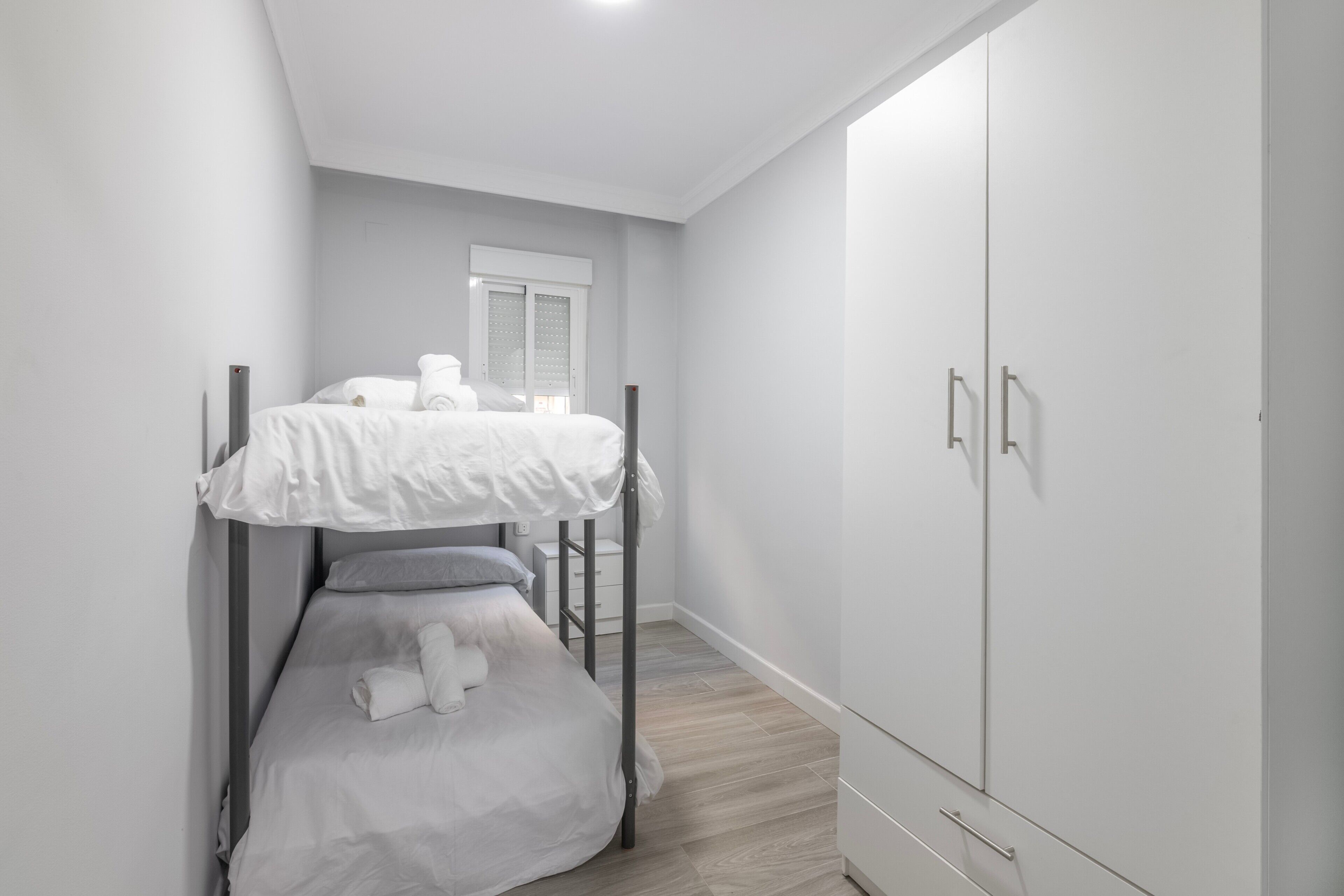 A bunk bed with white bedding, a wardrobe with a mirror, and a window with blinds.