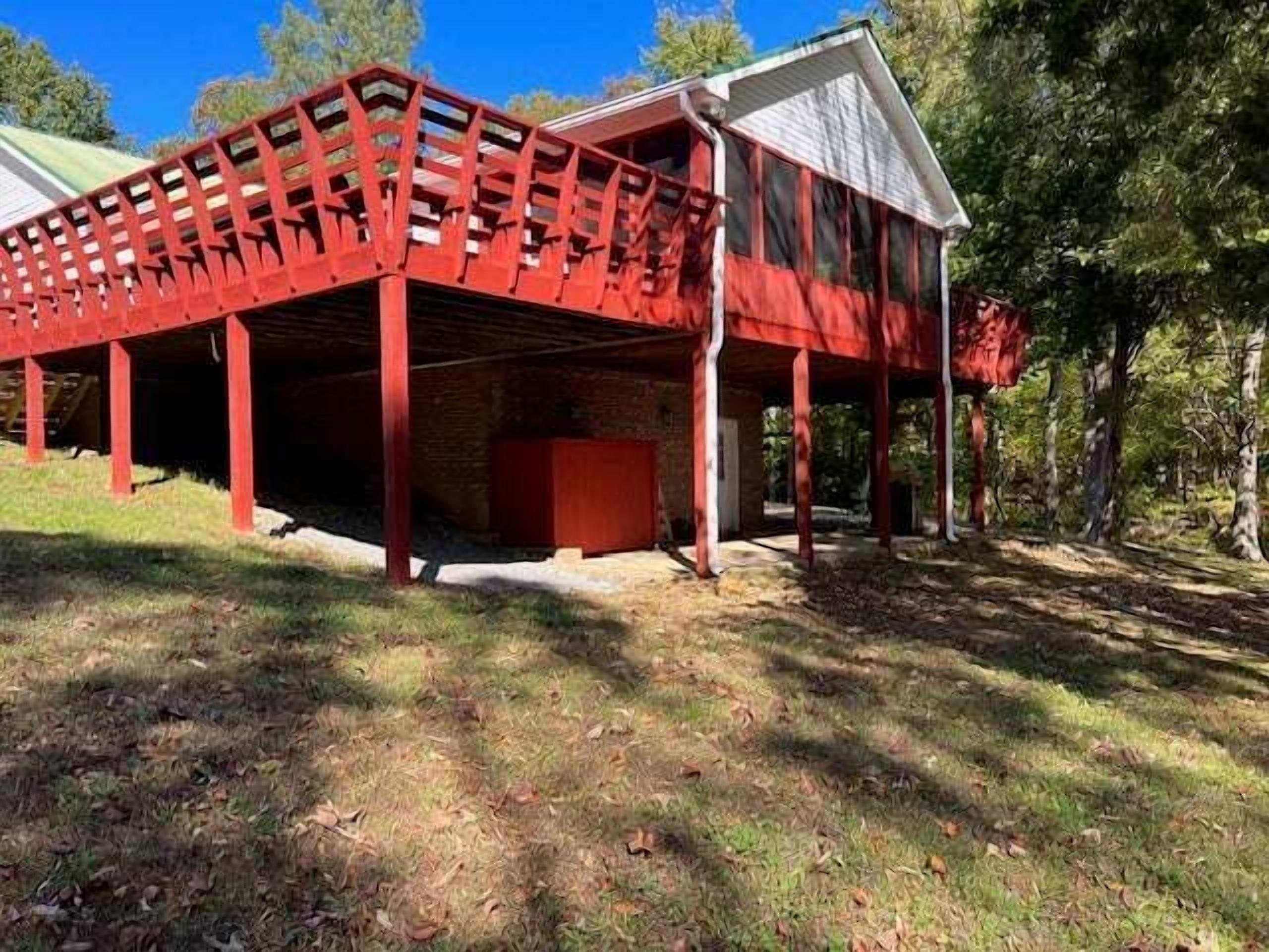 A red wooden structure with a covered porch, surrounded by trees and grass.