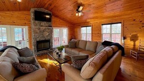 A cozy cabin interior with a stone fireplace, wooden walls, and a ceiling fan. - Cottage on Cypress Bay Near Paris Landing State Park (Buchanan)