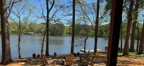 An outdoor seating area with wooden chairs and tables, overlooking a calm lake with trees in the background. - Cottage on Cypress Bay Near Paris Landing State Park (Buchanan)