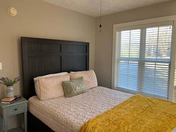 A bedroom with a bed, a nightstand, a window with blinds, and a ceiling light. - Cottage on Cypress Bay Near Paris Landing State Park (Buchanan)