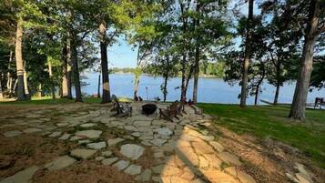A stone-paved area with a fire pit, surrounded by trees and a lake view.