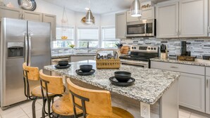 Una cocina moderna con una isla central, electrodomésticos de acero inoxidable y una barra de desayuno con sillas.