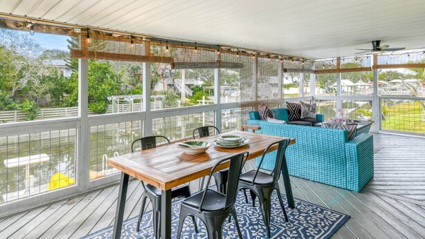 Un espacio al aire libre cubierto con una mesa y sillas de madera, un sofá azul y vistas a un cuerpo de agua y edificios.