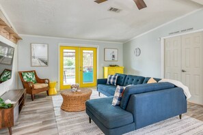 A living room with a blue sofa, wicker ottoman, and a yellow door leading outside.