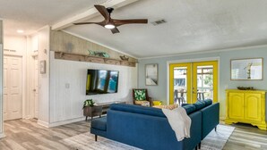 Una sala de estar con un sofá azul, un televisor, un ventilador de techo y un mueble amarillo.