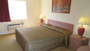 A hotel room with a bed, two bedside tables with lamps, a painting on the wall, and an air conditioning unit. - Starlite Motor Inn (Absecon)