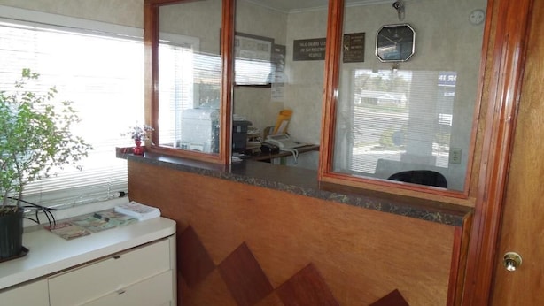 A room with a wooden accent wall, a window with blinds, a desk with a computer, and a potted plant. - Starlite Motor Inn (Absecon)