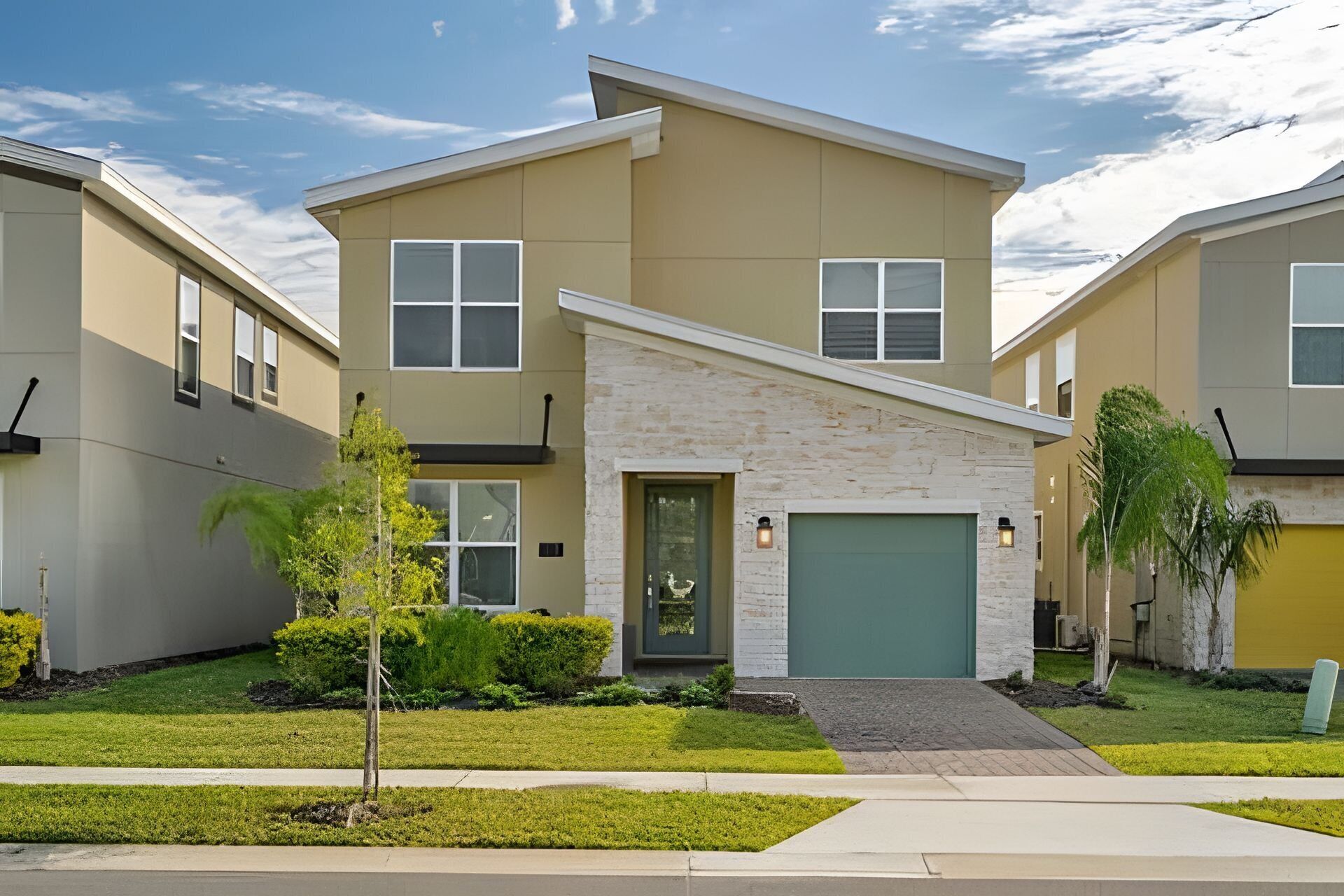 A modern two-story residential building with a stone facade, a green garage door, and a well-maintained lawn.