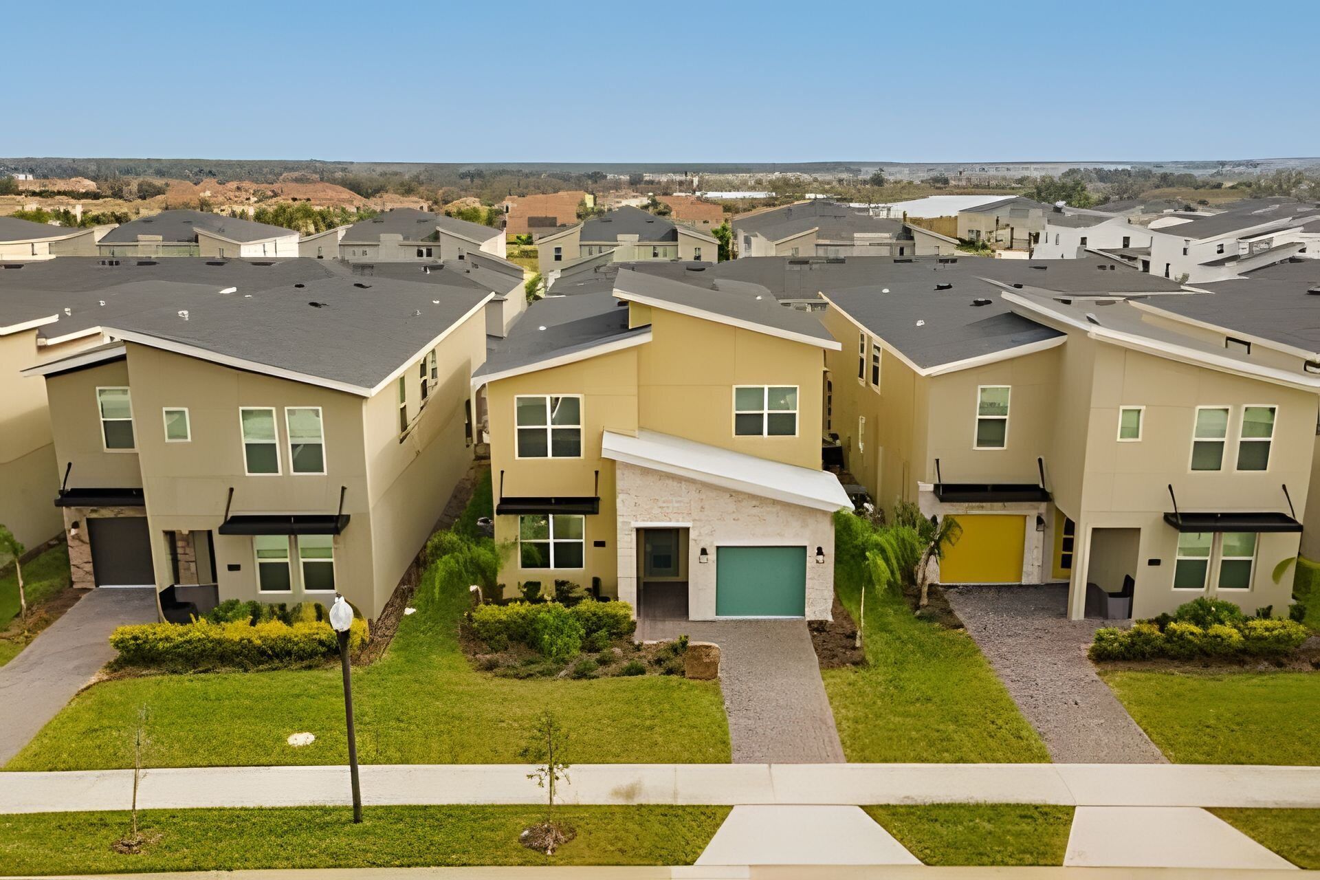 A row of modern townhouses with a central driveway, individual garages, and a landscaped front yard.