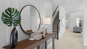 Een moderne hal met een houten consoletafel, een grote spiegel en een potplant. Een trap is op de achtergrond zichtbaar, die naar een andere kamer leidt.