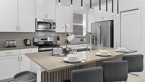 Een moderne keuken met witte kasten, roestvrijstalen apparatuur, een centraal kookeiland met zitplaatsen en hanglampen.