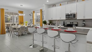 Une cuisine moderne avec des meubles blancs, des appareils en acier inoxydable et un îlot central doté de tabourets de bar.