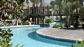 Une piscine au design incurvé, entourée de palmiers et dotée d’une terrasse en bois.