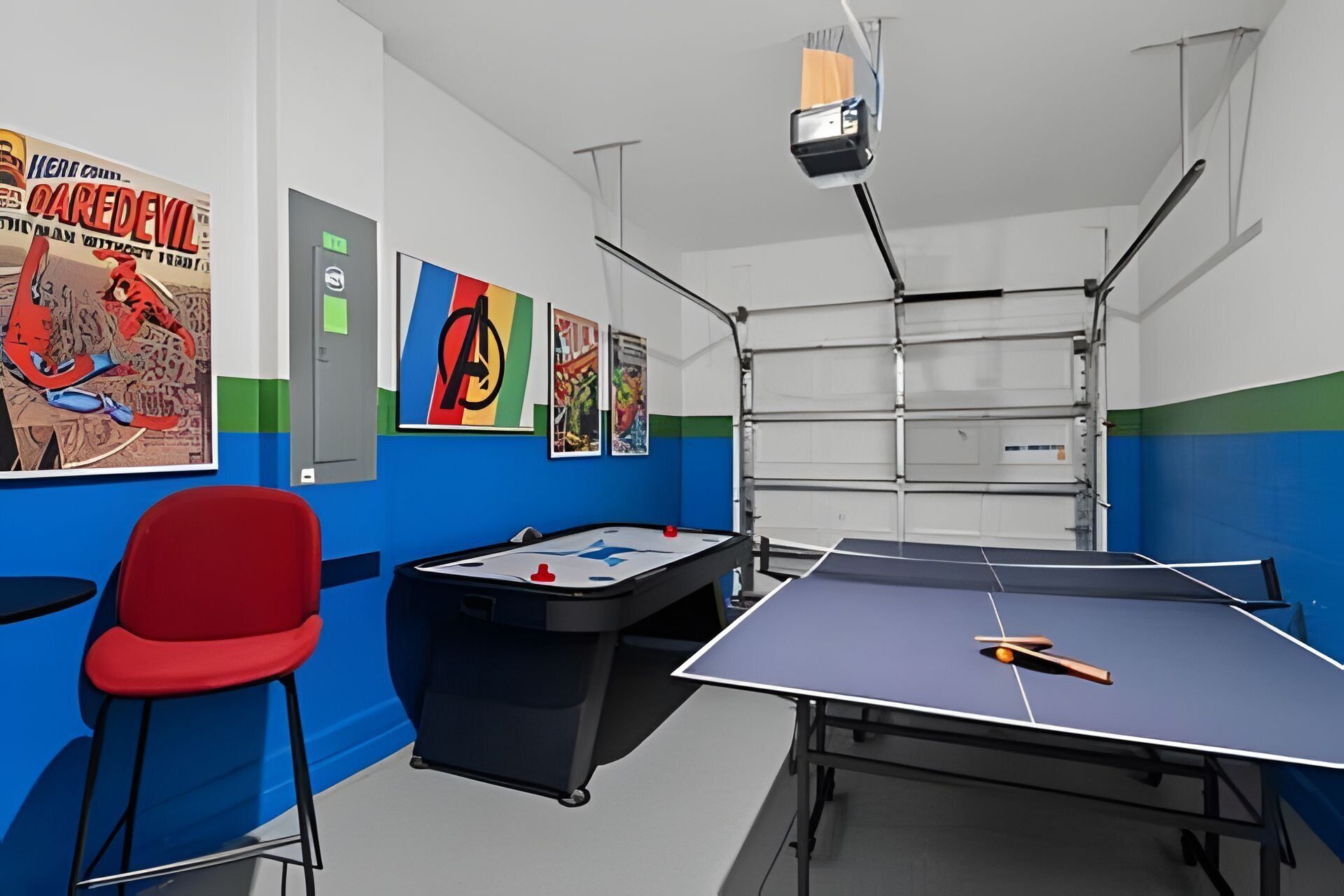 Une pièce avec une table de ping-pong, une chaise rouge et une table de billard. Les murs sont ornés de posters et un projecteur est fixé au plafond.