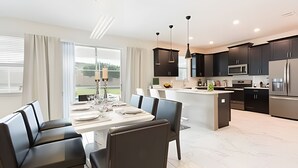 Una cocina moderna con armarios oscuros, una isla central y un comedor con mesa y sillas.