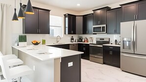 Una cocina moderna con gabinetes oscuros, electrodomésticos de acero inoxidable y una isla blanca.
