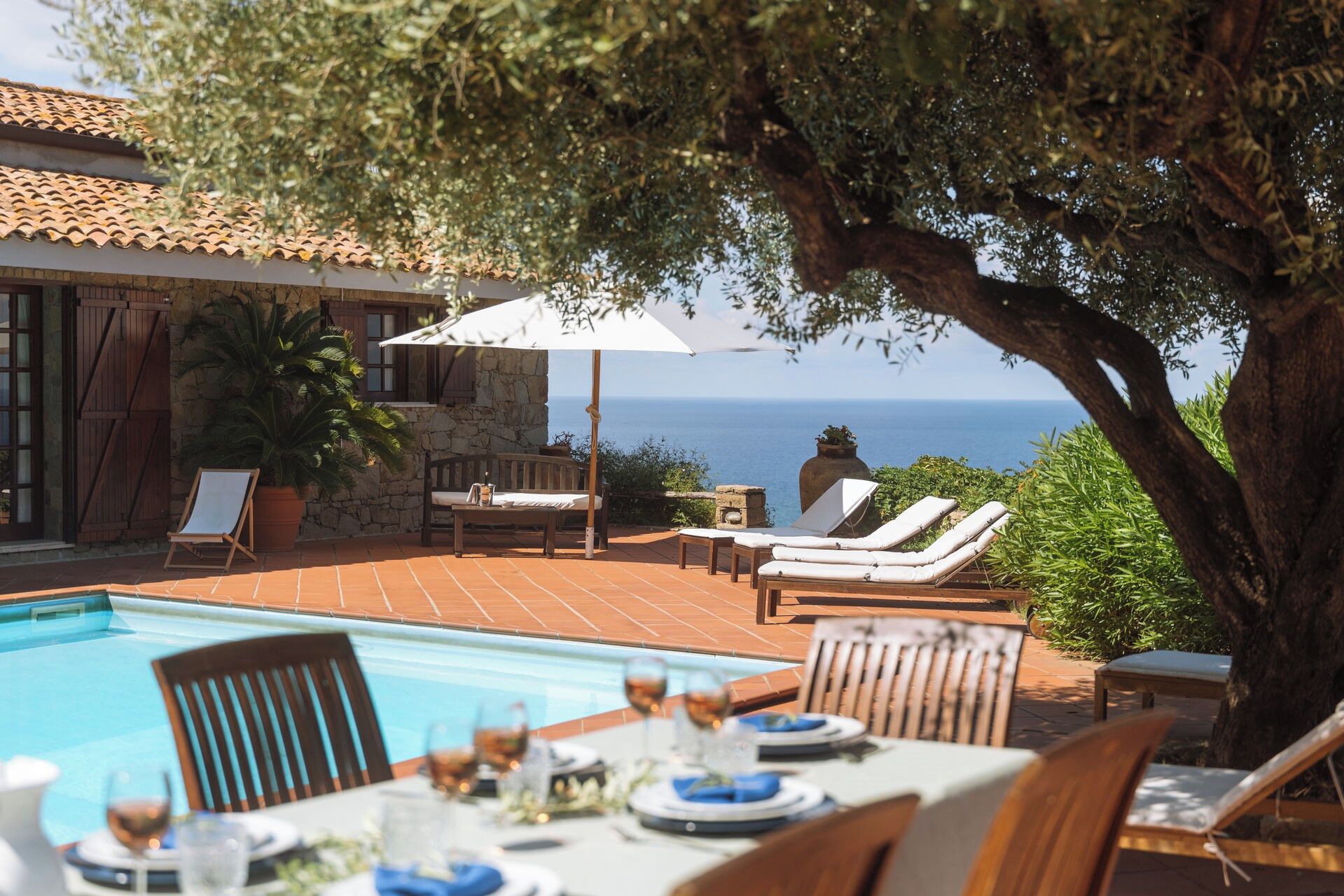 A poolside area with a table set for dining, lounge chairs, and a view of the sea.
