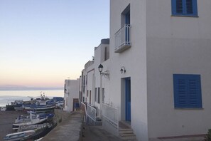 Ein Küstengebäude mit Balkon, Treppe und einer Reihe von Booten, die am Strand vor Anker liegen.