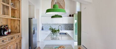 A modern kitchen with a wooden cabinet, a stainless steel refrigerator, a green pendant light, and a dining table with chairs.