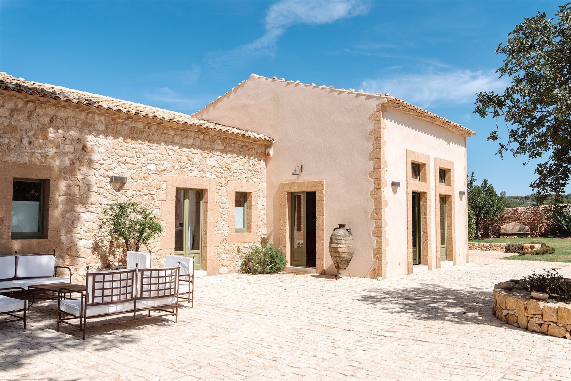 A stone building with a tiled roof, a large vase, and outdoor seating.