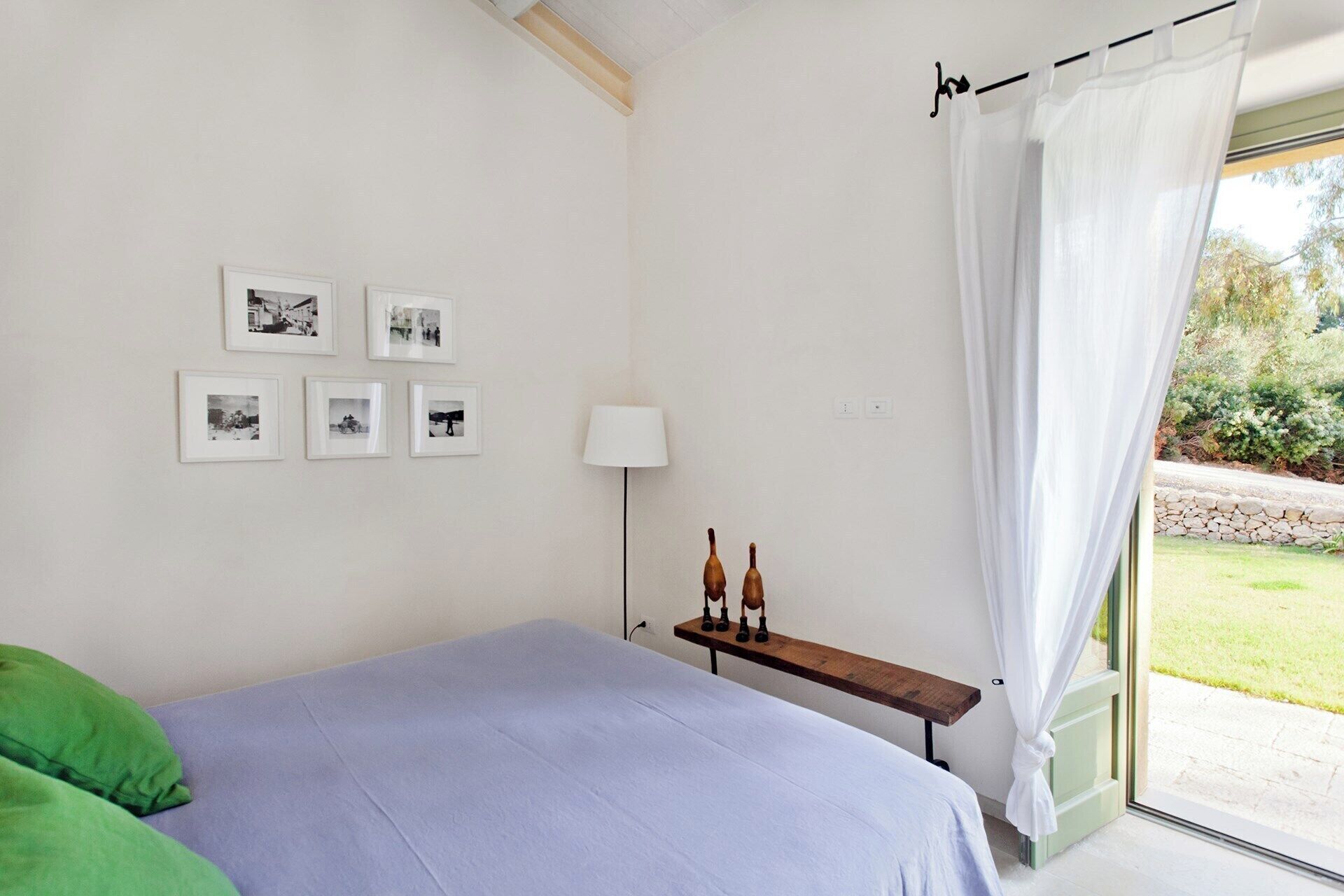 A bedroom with a bed, a bench with chess pieces, a lamp, and framed photos on the wall.