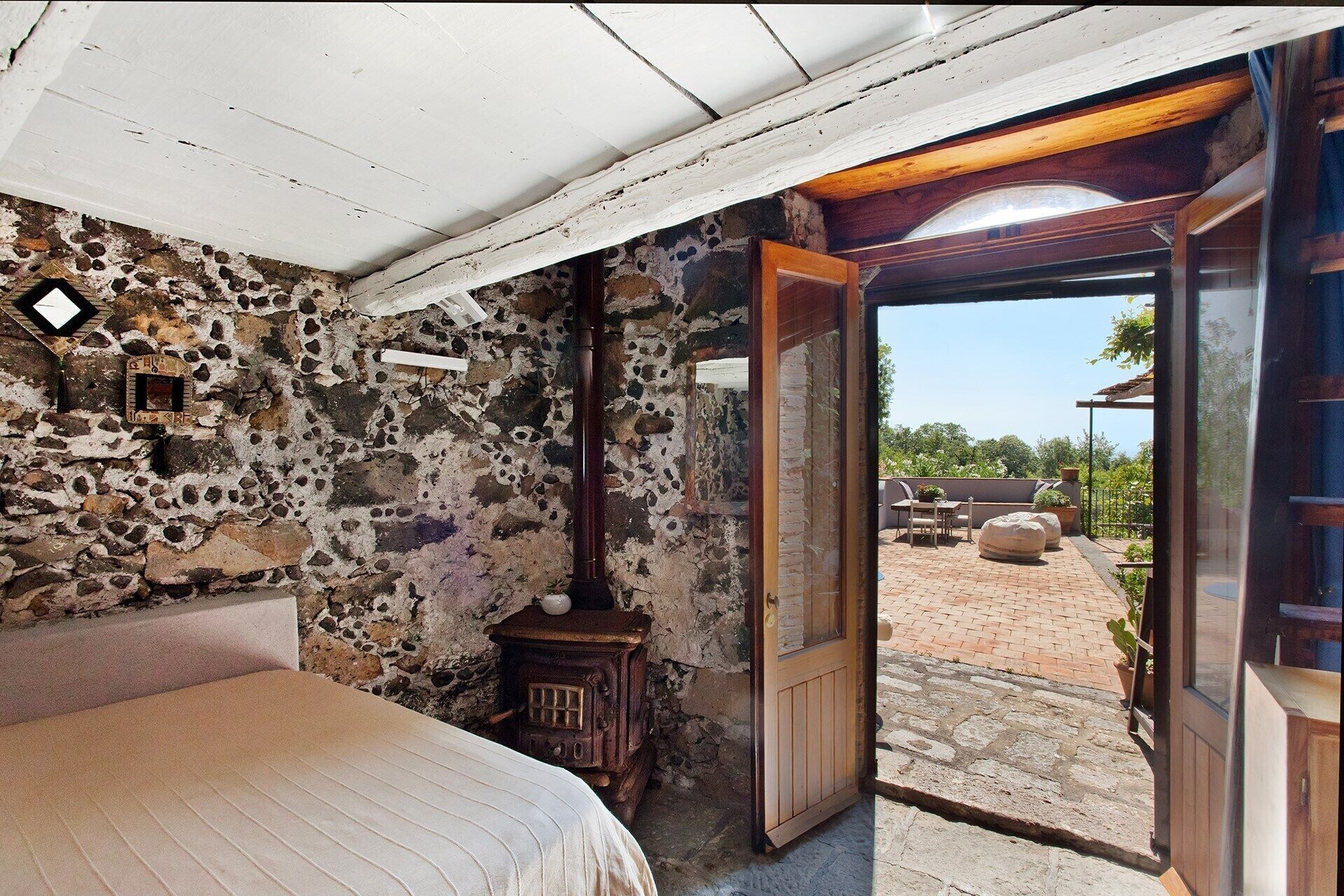 Una habitación rústica con pared de piedra, una cama, una puerta de madera y vistas a un patio exterior.
