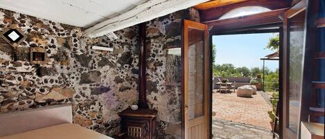Una habitación rústica con pared de piedra, una cama, una puerta de madera y vistas a un patio exterior.