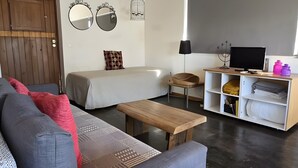 A modern living room with a wooden ceiling, a ceiling fan, a large flat-screen TV, a sofa, a bed, and a wooden bench. - Pedras Altas Apartment with Shared Pool (Castelo de Vide)