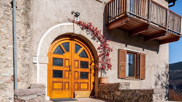 Un edificio con un gran puerta doble de madera, un balcón con barandillas de madera y un muro de piedra.