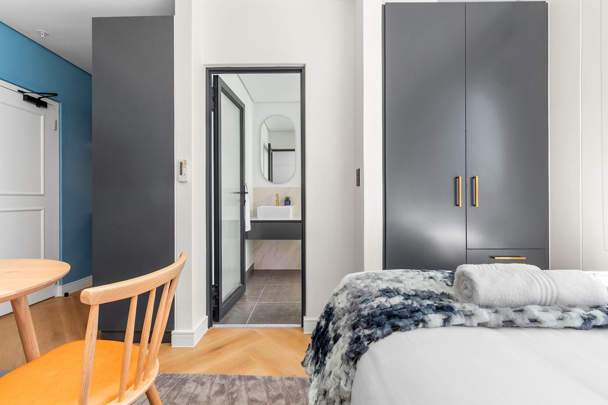 Quarto de hotel moderno com cama, uma cadeira de madeira, uma mesinha e um guarda-roupa.