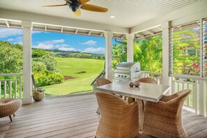 Eine überdachte Terrasse mit Grill, Korbmöbeln und Blick auf einen Golfplatz.