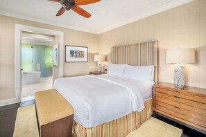 Ein Hotelzimmer mit einem Bett, einem Holznachttisch, einer Bank, einem Deckenventilator und einem durch eine offene Tür einsehbaren Badezimmer.
