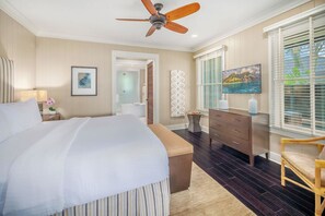 Une chambre à coucher avec un grand lit, un ventilateur de plafond, une commode, une chaise et un tableau au mur.