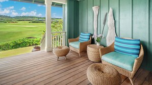 A covered porch with wicker furniture, a view of a golf course, and a green wall. - Golf Course View | Resort Amenities | Outdoor Shower (Koloa)