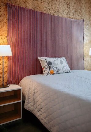 A bed with a quilted cover, a pillow with a leaf pattern, and a striped curtain.