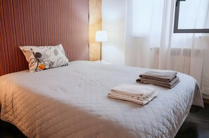A neatly made bed with a quilted blanket, a pillow with a leaf pattern, and folded towels on the bed.