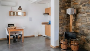A modern kitchen with a stone wall, a wooden dining table, and a television mounted on a stone pillar. - Rolhas Apartment with Shared Pool (Castelo de Vide)