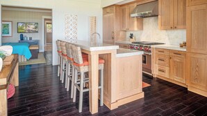 Een moderne keuken met houten kastjes, een centraal eiland en een eethoek met stoelen.