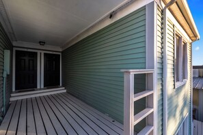 A wooden deck with a covered porch, a green exterior wall, and a white-framed window.