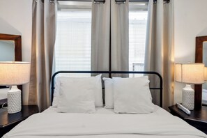 A neatly made bed with white linens and pillows, flanked by two bedside lamps on dark nightstands.