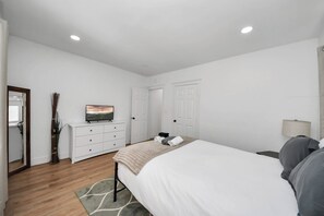 A bedroom with a bed, dresser, mirror, and a painting on the wall.