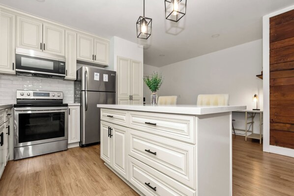 A modern kitchen with white cabinetry, stainless steel appliances, and a wooden floor.